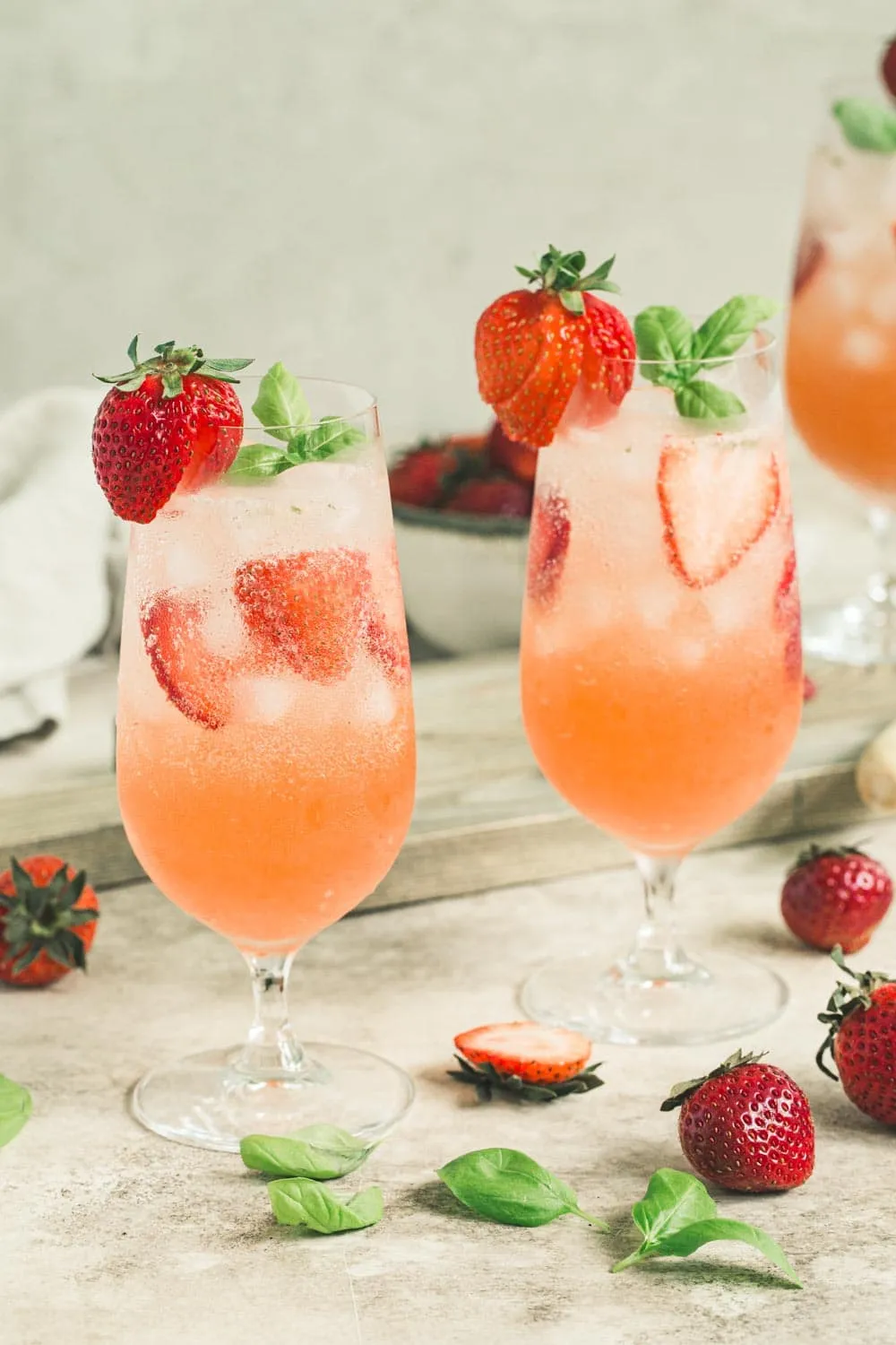 Two strawberry mojitos in tall clear glasses topped with sliced strawberries and basil leaves.