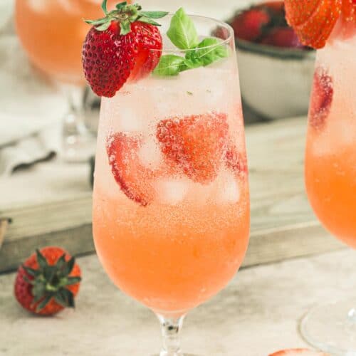 Strawberry mojito cocktail in tall clear glass with fresh sliced strawberries and basil leaves.