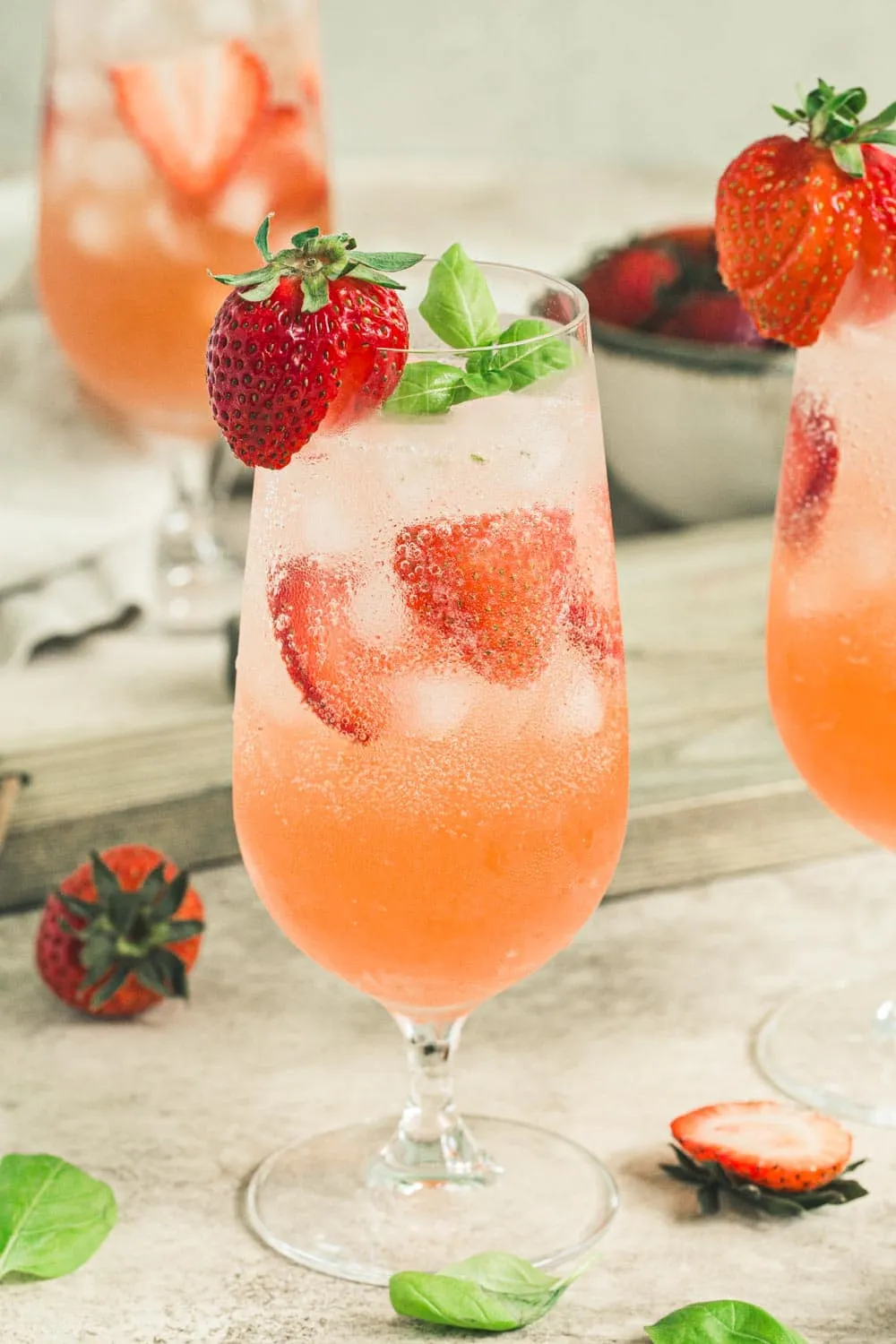 Strawberry mojito cocktail in tall clear glass with fresh sliced strawberries and basil leaves.