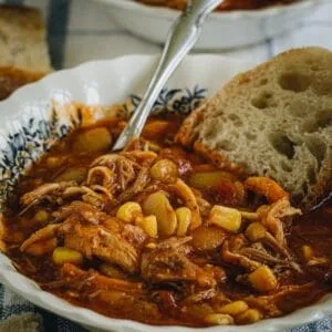 Side view of Brunswick stew in a white bowl with blue flowers and slice of bread.