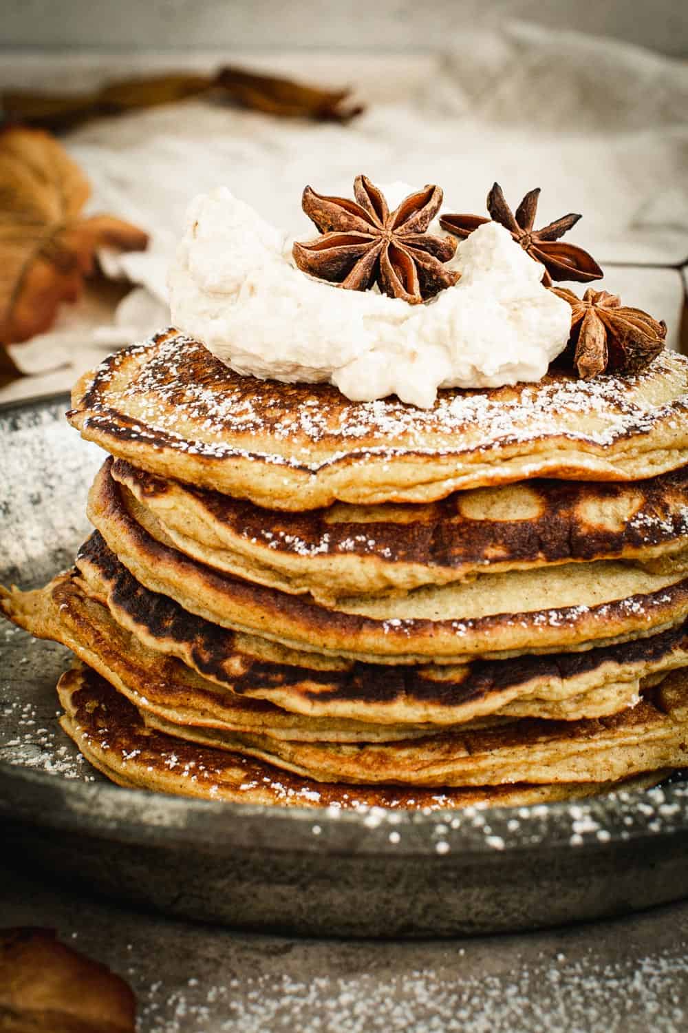Pumpkin pancakes stacked and covered in powdered sugar and topped with whipped cream.