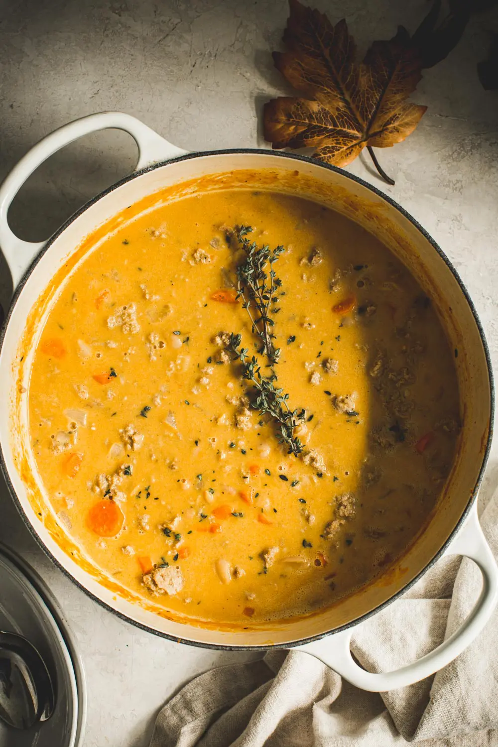 Pumpkin white bean chili in large white Dutch oven with sprig of fresh thyme.