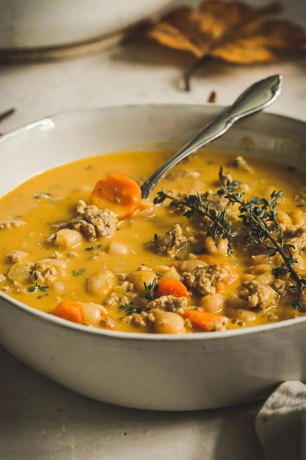 Close of view of a bowl of turkey pumpkin white bean chili in a white bowl.