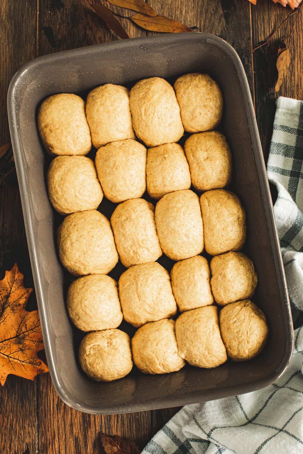 Unbaked pumpkin dinner rolls in a gray baking dish.