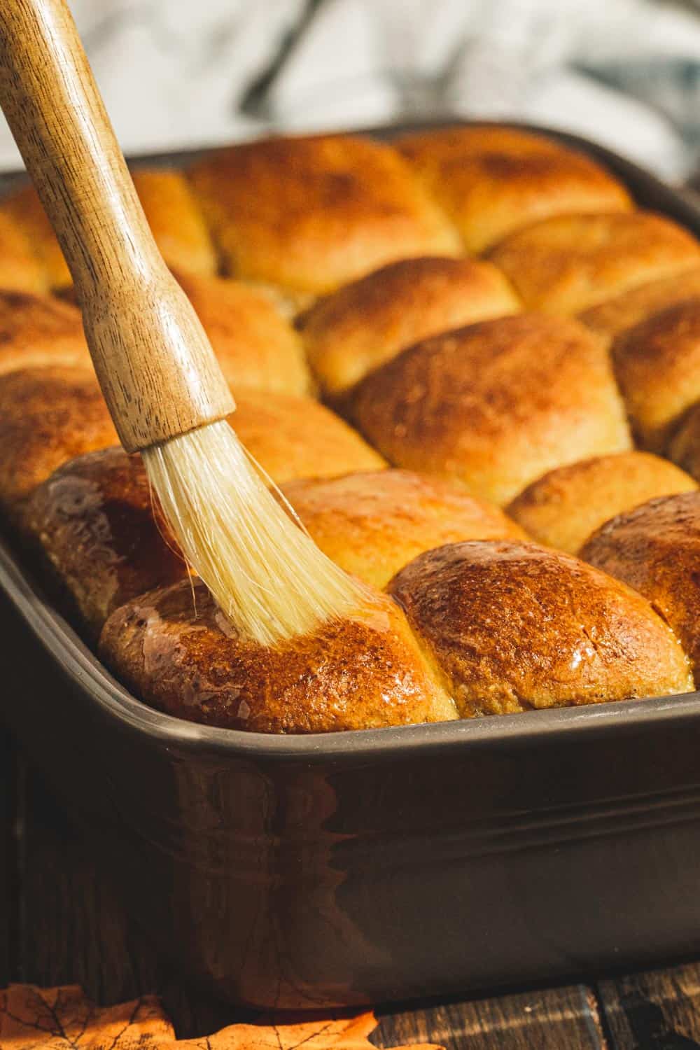 Brushing butter on top of pumpkin rolls in a baking dish.