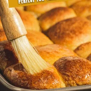 Pumpkin dinner rolls being brushed with butter. Image with white title.