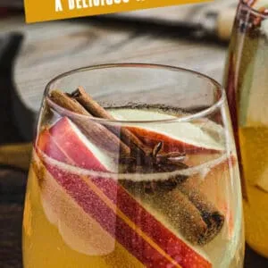 Caramel apple cider sangria in a stemless glass with apple slices and a cinnamon stick. Pinterest image with white title.