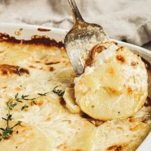 Scalloped potatoes in a white dish with a silver serving fork taking out a serving.