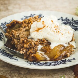 Apple dump cake on a white and blue plate topped with cinnamon whipped cream.