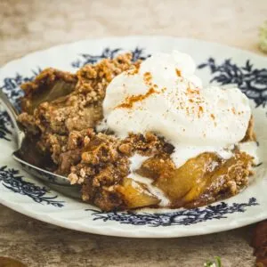 Apple dump cake on a white and blue plate topped with cinnamon whipped cream.