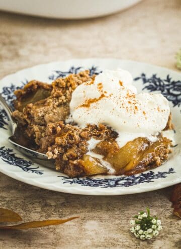 Apple dump cake on a white and blue plate topped with cinnamon whipped cream.