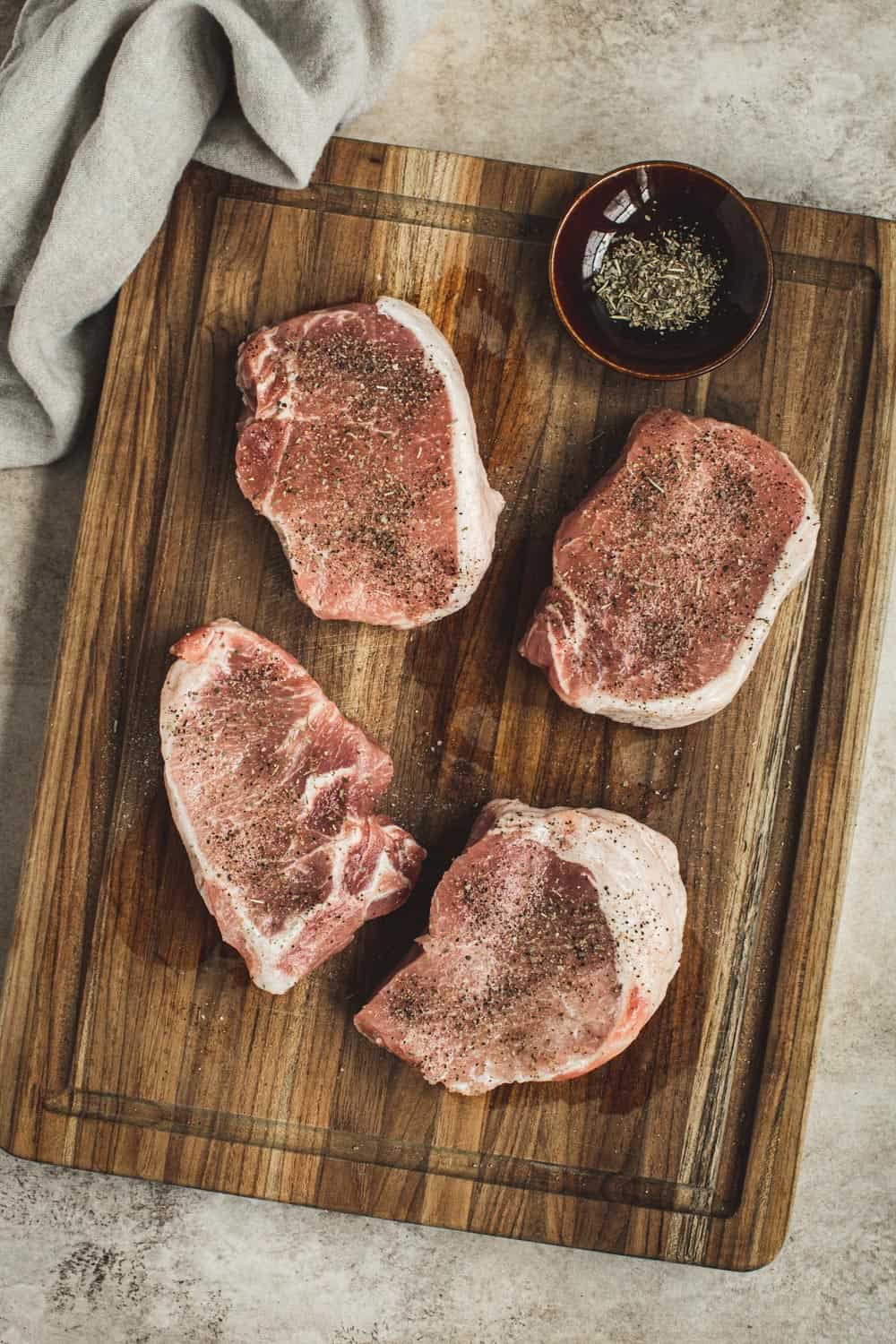 Seasoned pork chops on a wooden cutting board.