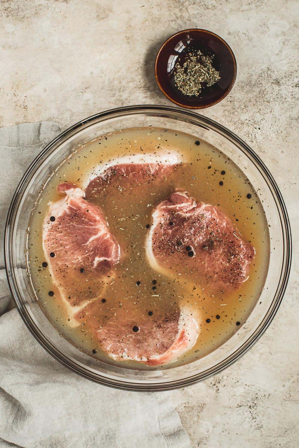 Pork chops in an apple cider brine in a glass mixing bowl.