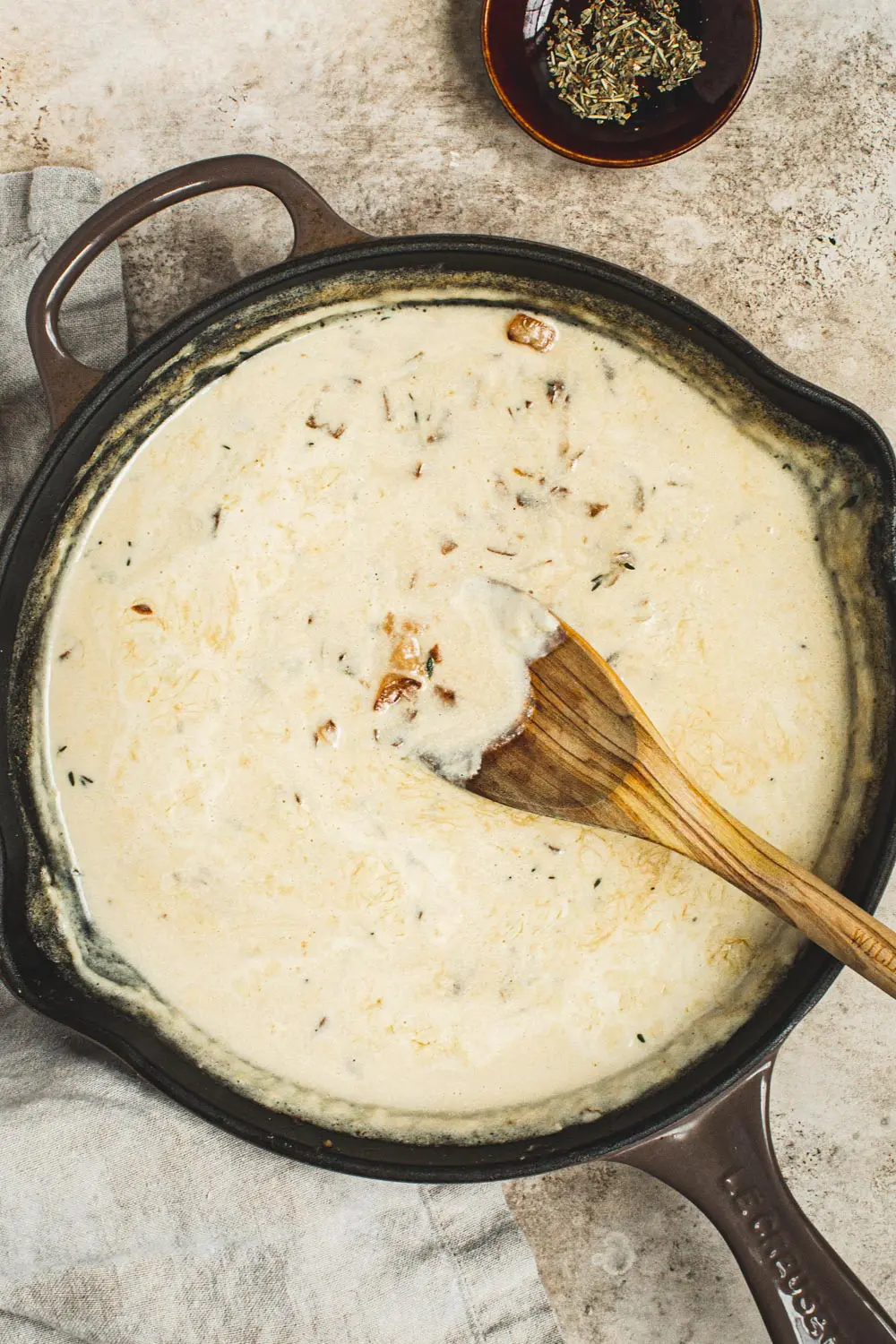 Apple cider cream sauce in a skillet with a wooden spoon.