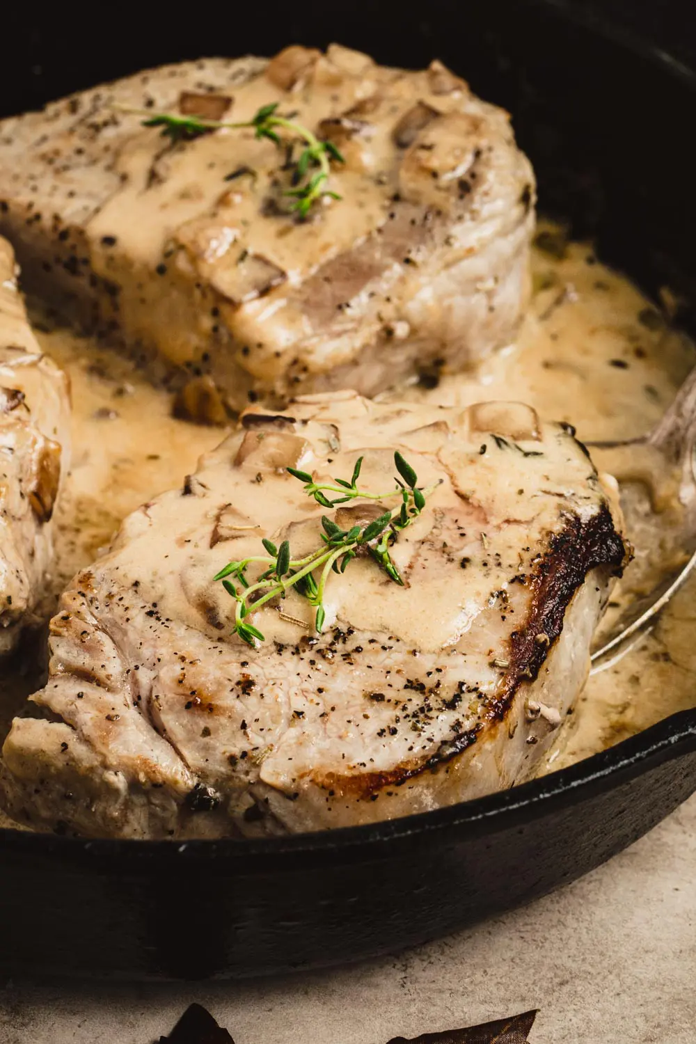 Apple cider brined pork chops in an apple cider cream sauce topped with fresh thyme in an iron skillet.