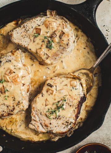 Pork chopes in a creamy apple cider sauce topped with fresh thyme in an iron skillet.