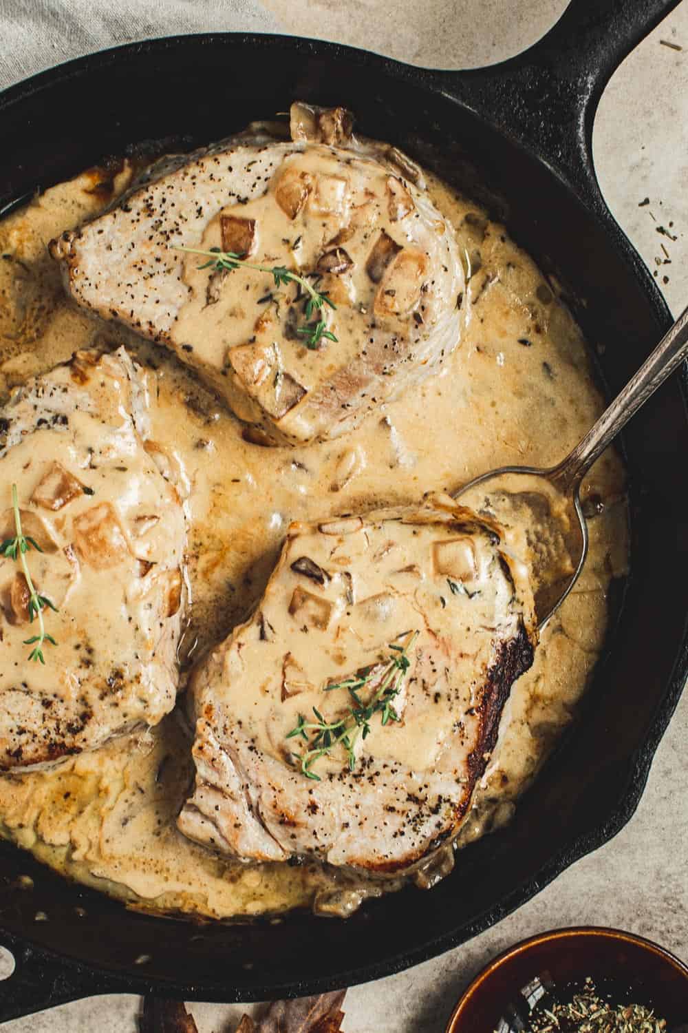 Pork chopes in a creamy apple cider sauce topped with fresh thyme in an iron skillet.