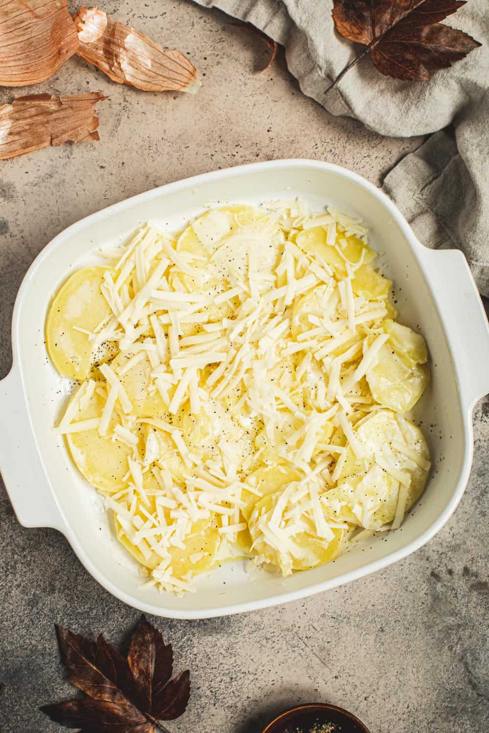 Shredded cheese over sliced potatoes in a square baking dish.