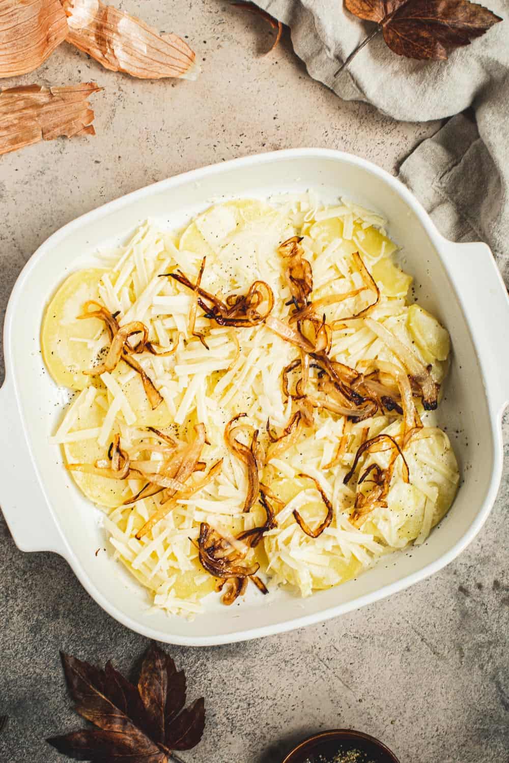 Sautéed onions and cheese over sliced potatoes in a square baking dish.