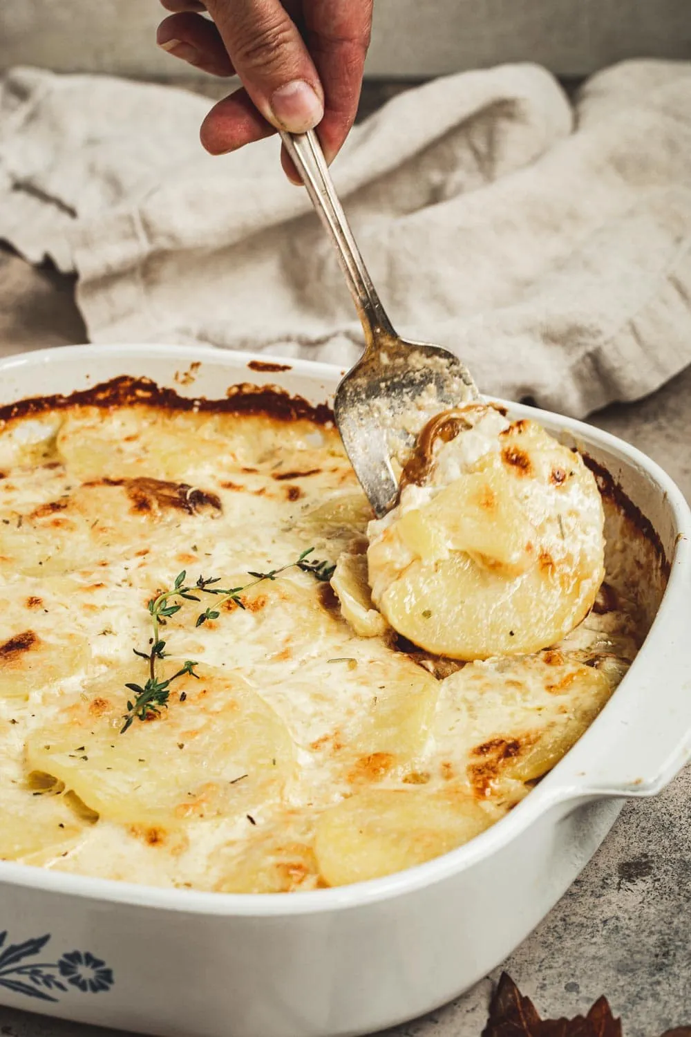 Serving fork scooping out scalloped potatoes from baking dish.