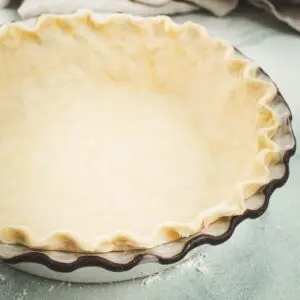 Homemade flaky pie crust set up in a white pie dish.