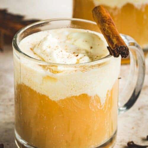 Caramel Bourbon Apple Cider Cocktail in a glass coffee mug topped with whipped cream and a cinnamon stick.