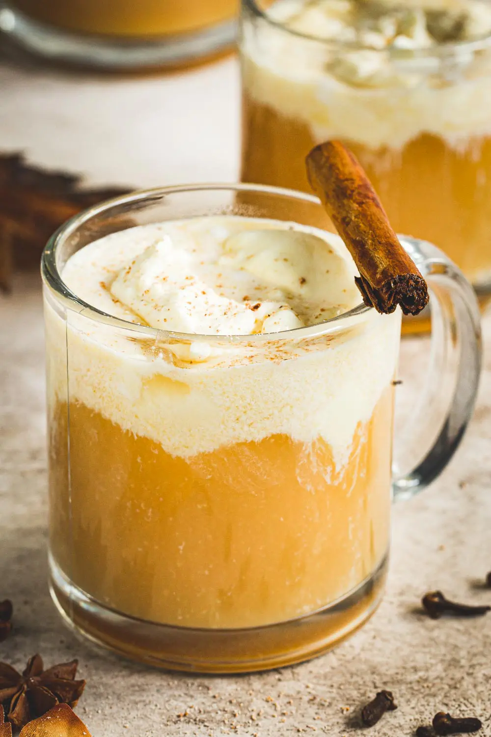 Caramel Bourbon Apple Cider Cocktail in a glass coffee mug topped with whipped cream and a cinnamon stick.