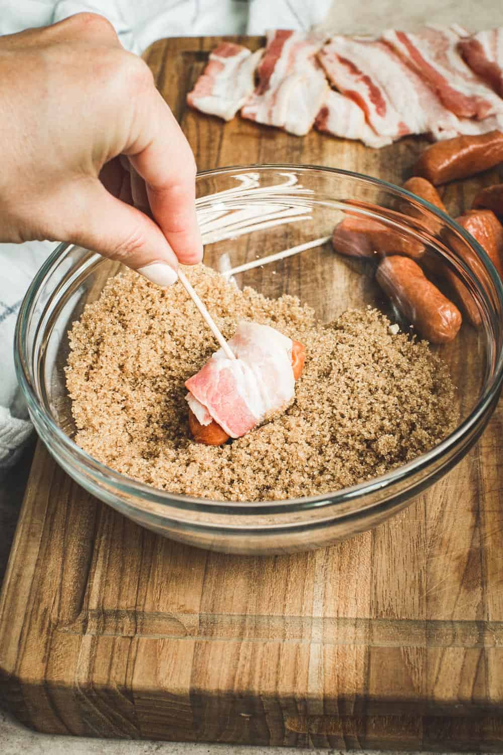 Hand dipping little smokies into brown sugar mixture in a glass bowl.