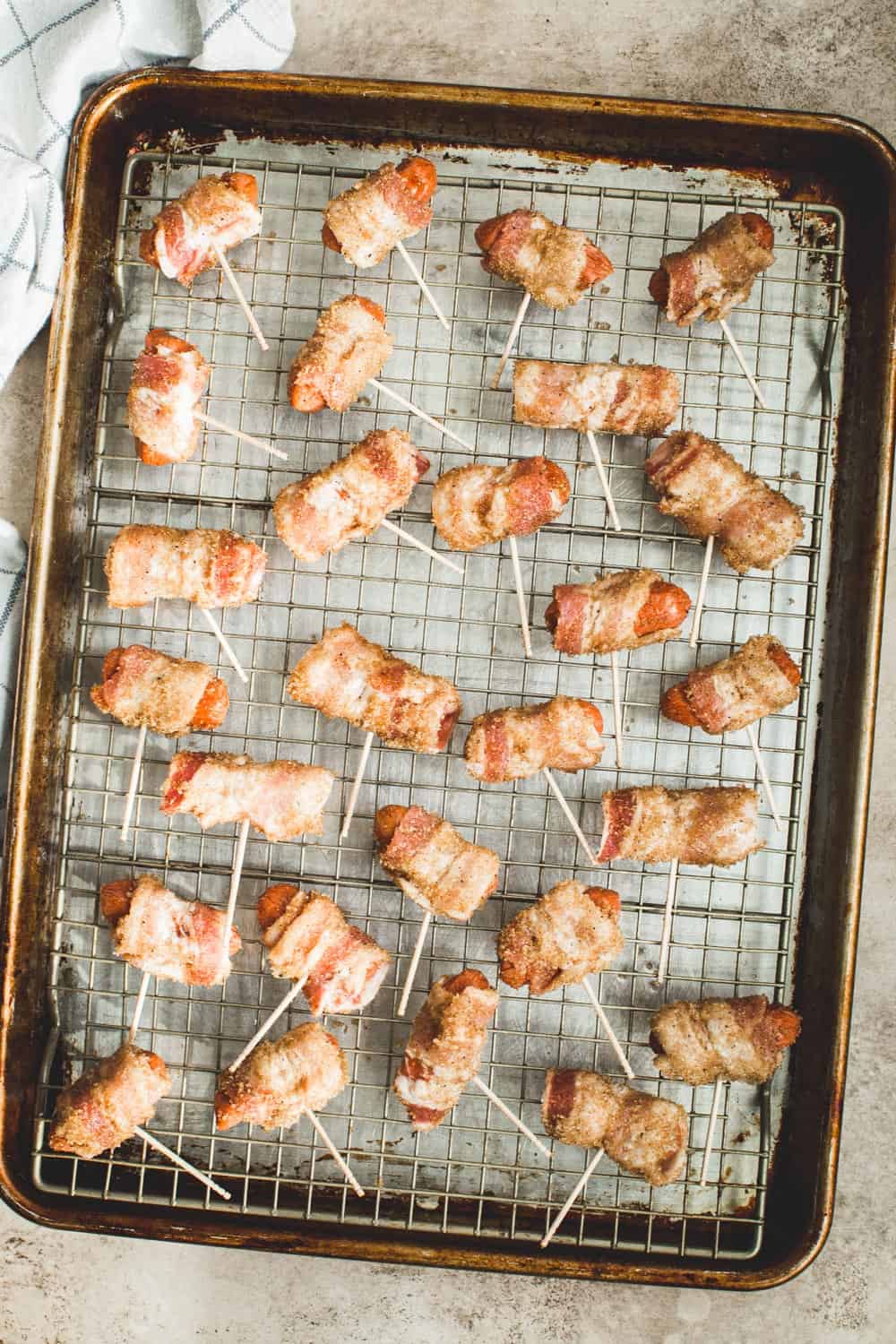 Little Smokies wrapped in bacon on a wire rack sitting on a rimmed baking sheet.