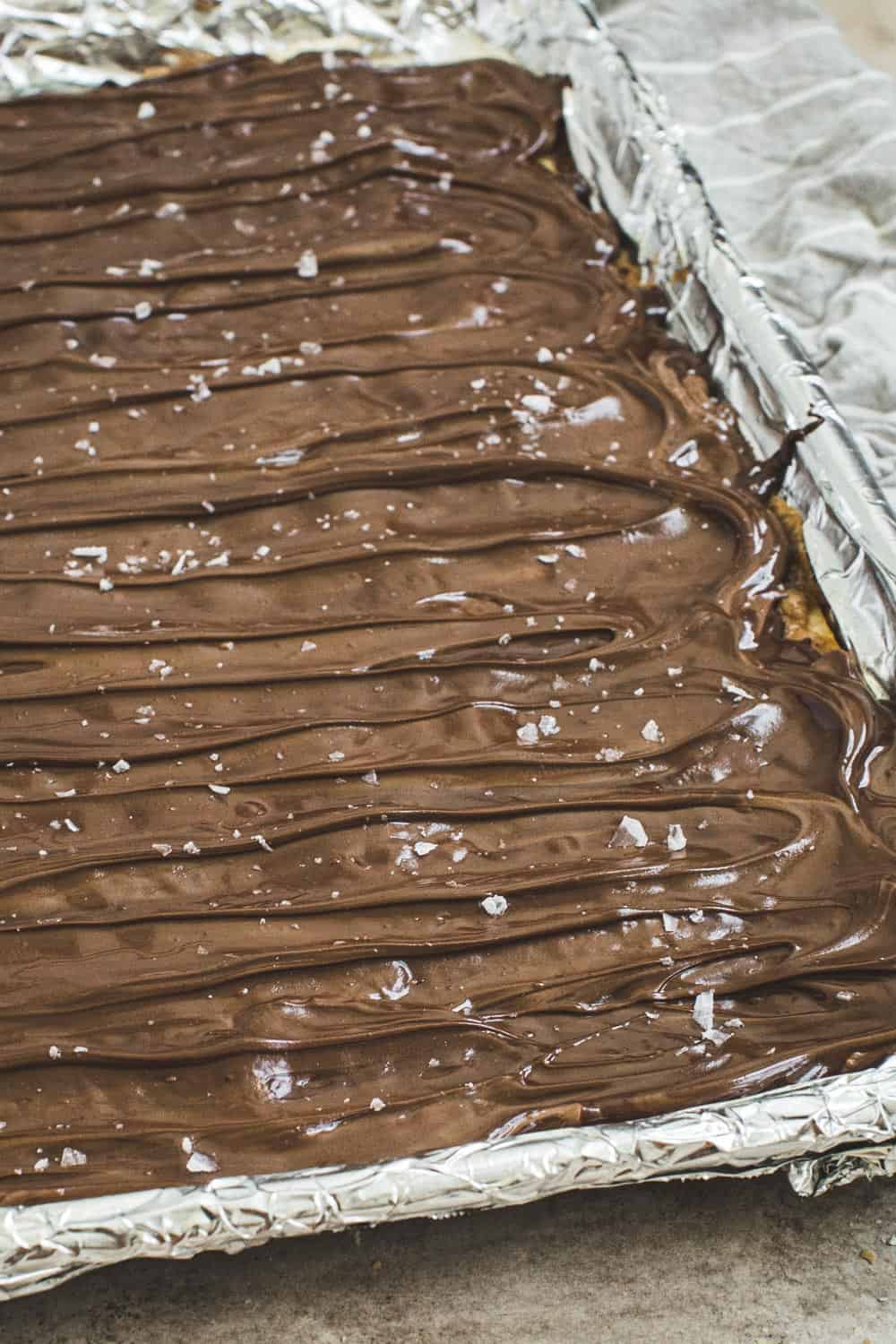 Melted chocolate spread on top of saltine bark with salt flecks.