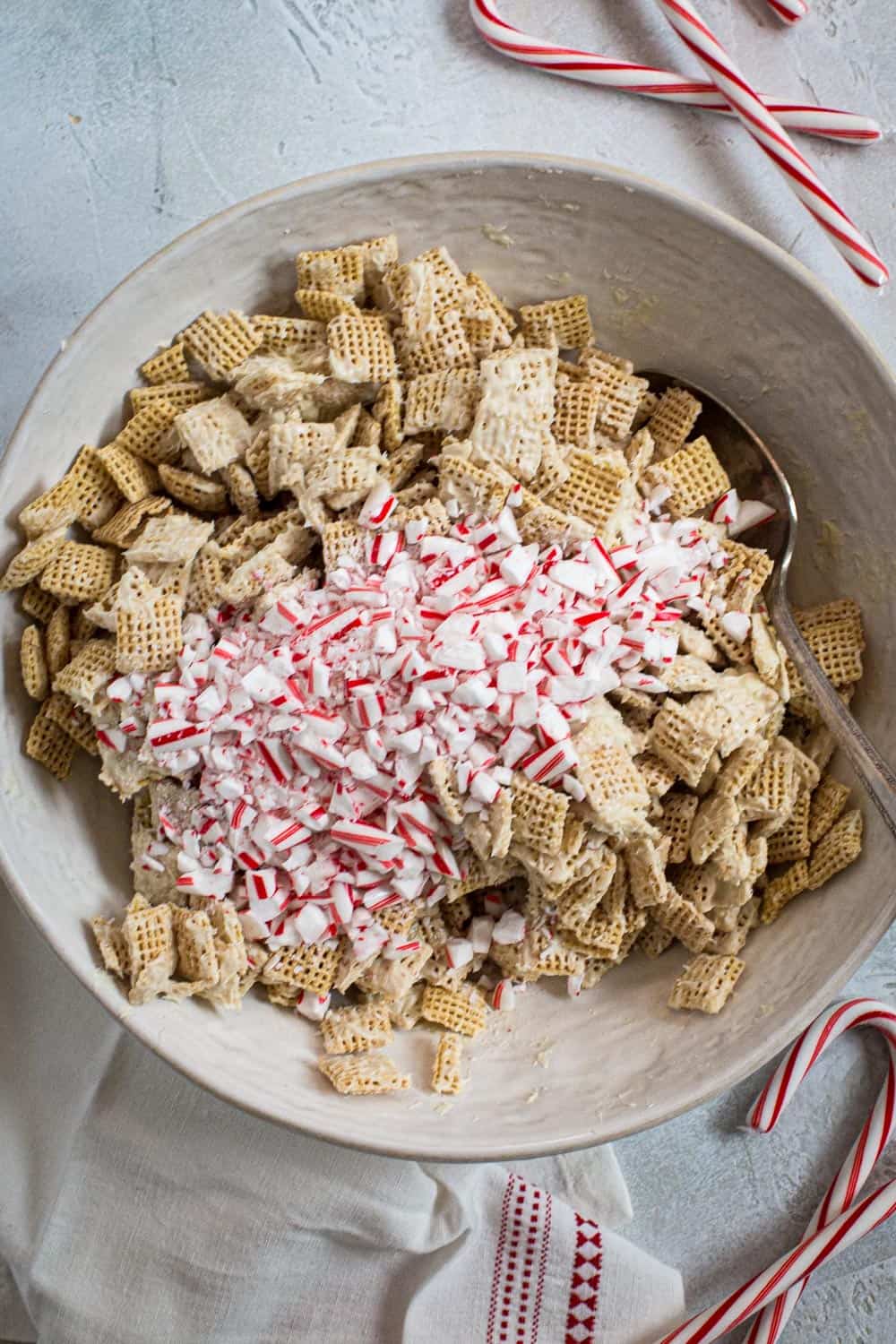 Crushed peppermint on top of puppy chow mixture in a mixing bowl.