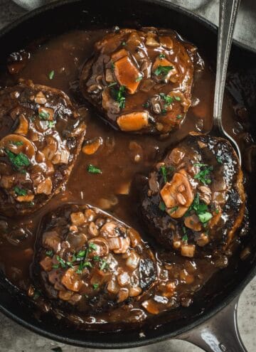 Easy skillet salisbury steak in a cast iron skillet with a silver serving spoon scooping up a steak.