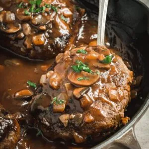 Skillet salisbury steak with a silver spoon scooping one up.