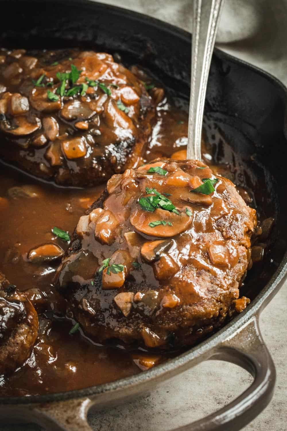 Skillet salisbury steak with a silver spoon scooping one up.
