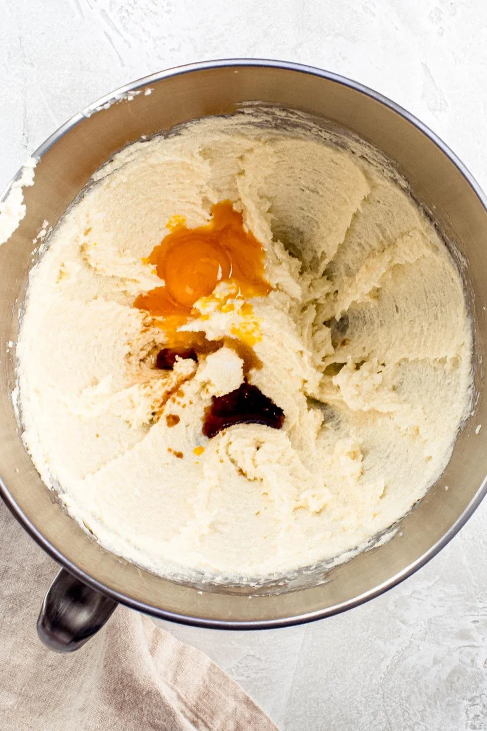 Egg mixed into cookie batter in silver mixing bowl.