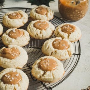 Dulce de Leche Thumbprint cookies on a round wire rack with sauce in a jar behind them.