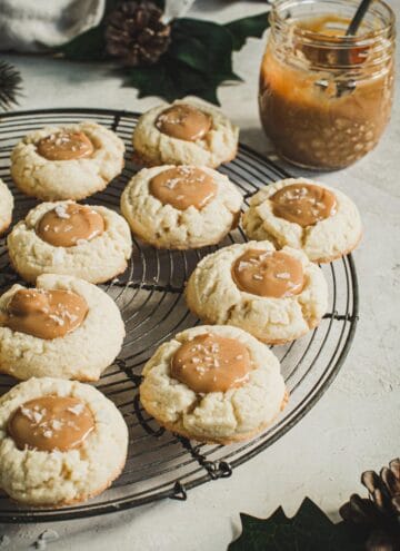 Dulce de Leche Thumbprint cookies on a round wire rack with sauce in a jar behind them.