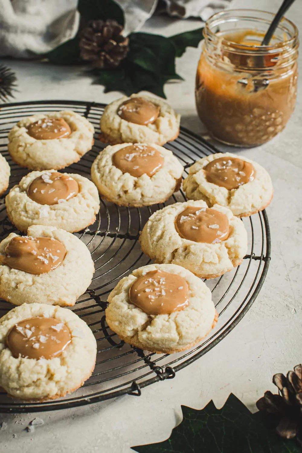 Dulce de Leche Thumbprint cookies on a round wire rack with sauce in a jar behind them.