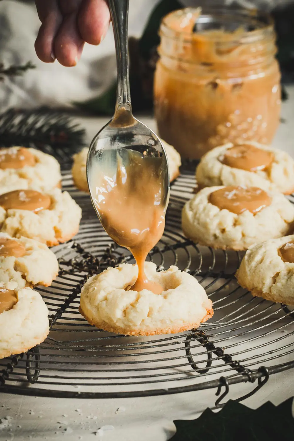 Spoon dripping dulce de leche into thumbprint cookies.
