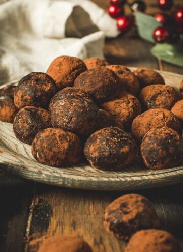 Chocolate rum balls stacked on a wooden plate.