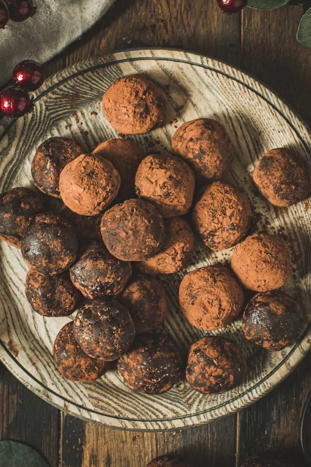 Rum balls coated in cocoa powder on a wooden plate.