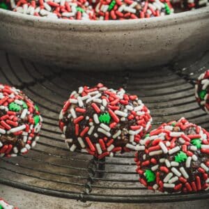 Old fashioned rum balls coated in Christmas sprinkles on a wire rack.