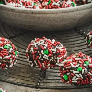 Old fashioned rum balls coated in Christmas sprinkles on a wire rack.