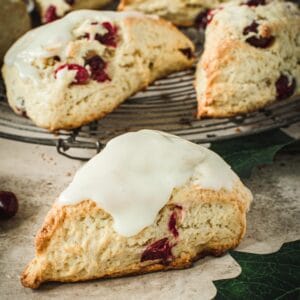 Cranberry orange scone covered in an orange glaze with scones behind it on a wire rack.