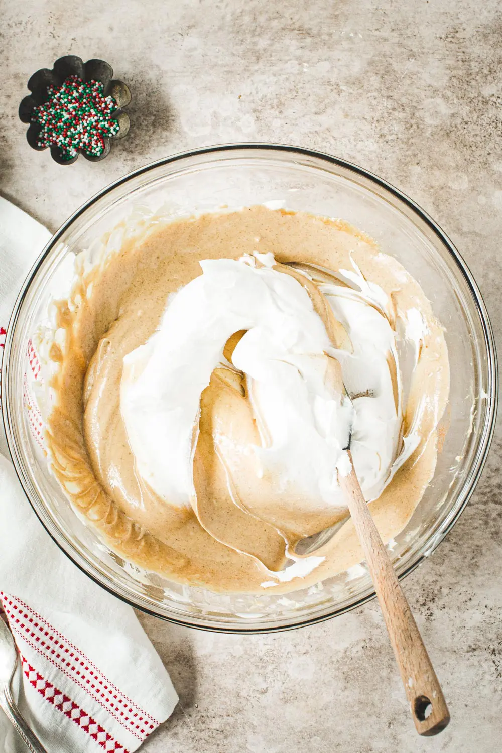 Folding cool whip into gingerbread dip ingredients in a glass bowl.