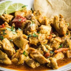 Creamy coconut chicken curry close up garnished with cilantro and lime wedges.