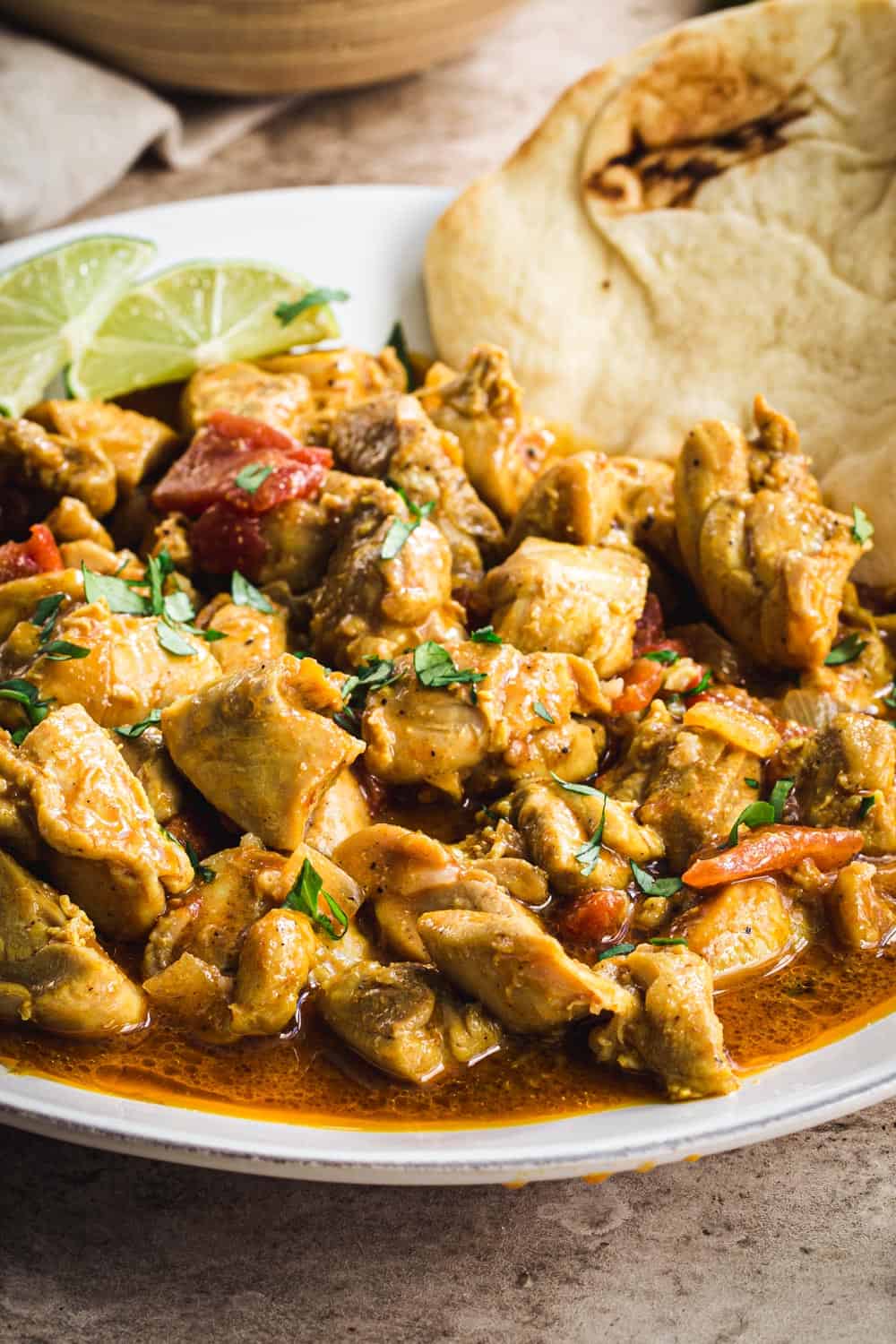 Creamy coconut chicken curry close up garnished with cilantro and lime wedges.