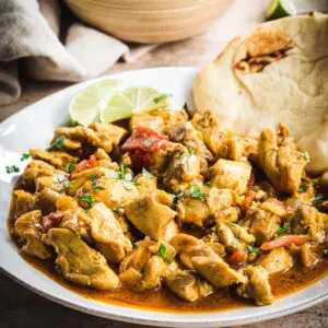 Creamy coconut chicken curry on a white plate with Naan and lime wedges.