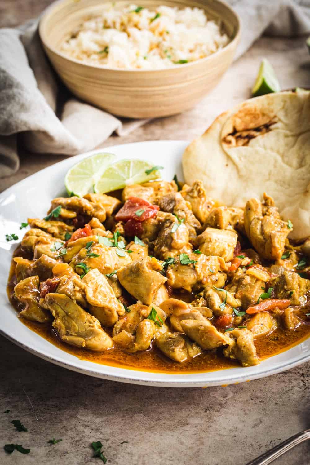 Creamy coconut chicken curry on a white plate with Naan and lime wedges.