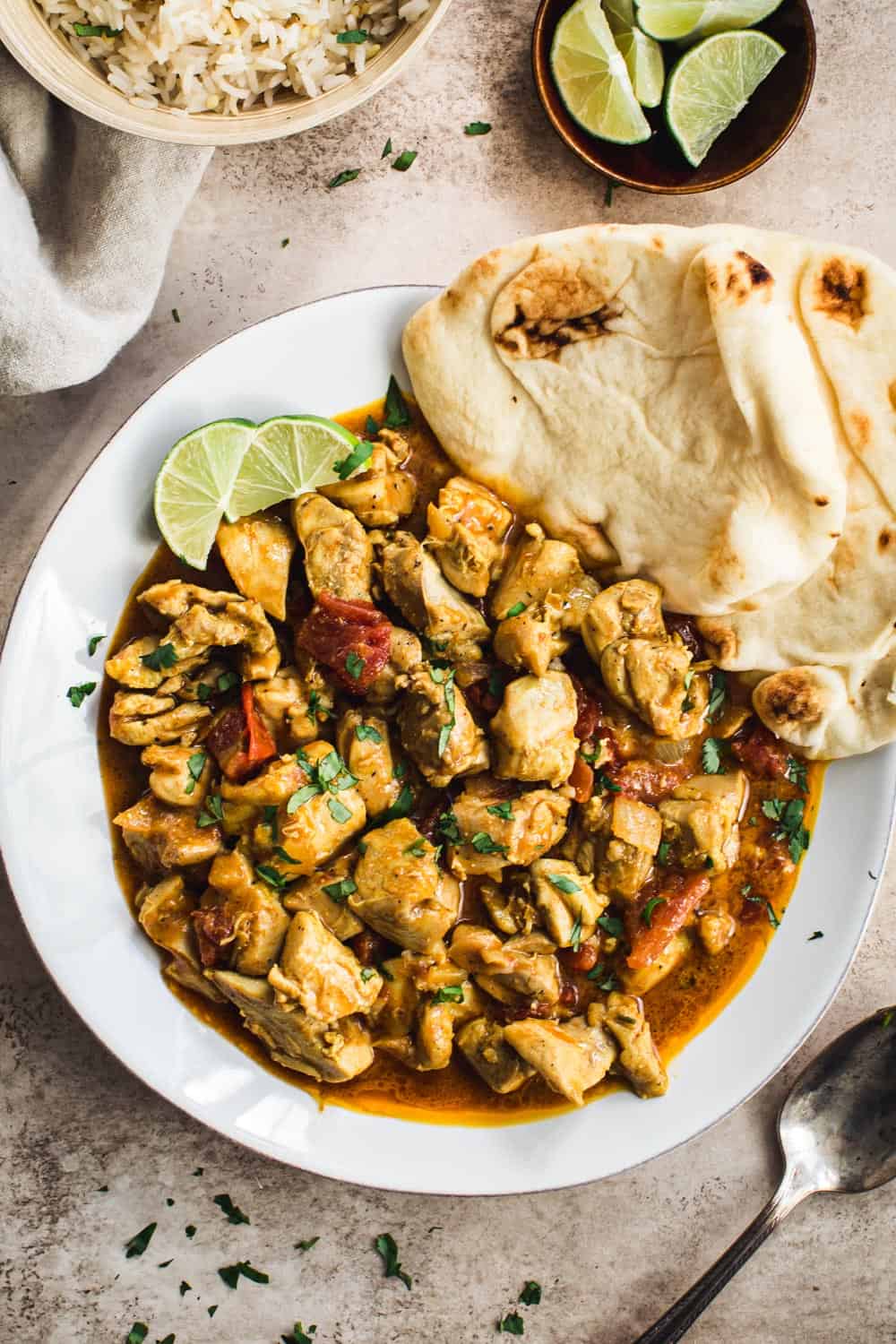 Creamy coconut chicken curry with Naan and lime wedges on a white plate.